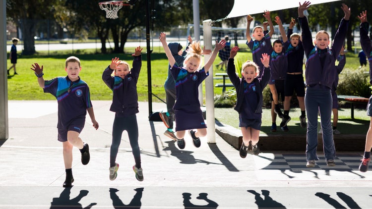 Students jumping up outside in playground.