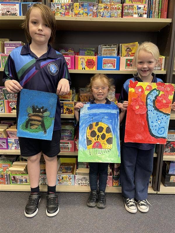 Three students holding artworks.