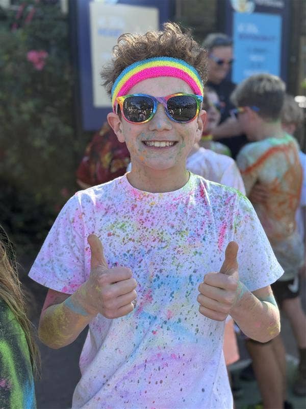 Stuent in rainbow headband covered in colourful dust